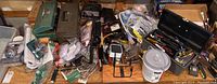 Overview of the entire lot on a wooden surface showing toolboxes, small packages, bulbs, hardware items, and a plastic bucket with tools.