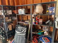 Three gray metal utility shelves inside garage. Shelves hold various items but are to be sold empty. Shelving is industrial style with steel frames and solid shelves.