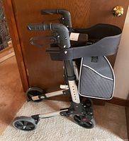 Medic Therapeutics walker folded against a door, showing side view with seat and storage bag.