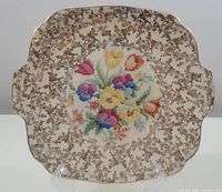 Front view of 1930's H&K Tunstall ceramic plate with floral center and ornate brown border.