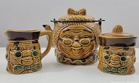 Full set view of teapot, creamer, and sugar bowl with matching character faces and brown glaze.