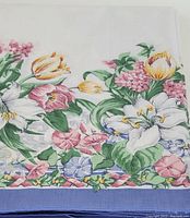 Section of floral pattern showing pink, yellow tulips, white lilies, and green leaves with blue border edge.