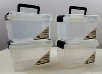 Photo shows four transparent plastic storage bins stacked in two columns. Bins have black handles and snap-on lids with side clips. Each bin has a front label stating 'PERSP STORAGE'.