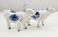 Side view of two cow-shaped Delft blue creamers showing the hand painted floral patterns and overall shape