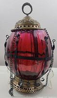 Full front view of ruby glass hanging fixture with brass cap and base, iron cage and chains
