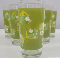Front view of one drinking glass showing green frosted band and tulip silkscreen design with five additional glasses blurred in the background.