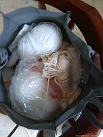 Top-down view inside a grey bag showing multiple white yarn balls and skeins of varying sizes, some wrapped in plastic.