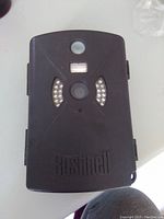 Front view of closed Bushnell Trail Sentry trail camera showing black casing with lens, motion sensor, and infrared LED lights around the lens. Bushnell branding on lower front.