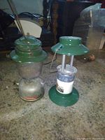 Photo showing two Coleman propane lamps side by side on the floor, one missing the glass globe.