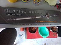 Box packaging with the label 'Hunting Knife ART NO. CK163 Stainless Steel Blade' and decorative blade image.