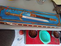 Decorative sword in an ornate gold-trimmed blue velvet frame showing blade and handle