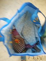 Photo shows mixed fabrics inside a blue reusable shopping bag including blue and multi-colored patterned fabrics.