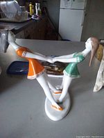 Photo showing two porcelain figurines of girls dancing, one in orange dress and the other in green, both mounted on a shared base.