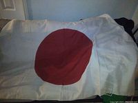 Image showing a white flag with a central large red disc spread out on a surface.