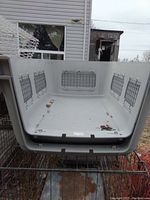 Interior view of large white plastic dog crate base showing metal ventilation grids on sides and dirty bottom with no connectors present.