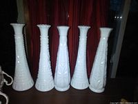 Photo showing five vintage milk glass vases arranged in a row against a red curtain background, highlighting different raised patterns and shapes.