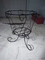 Front view of black metal wire plant stand showing curved legs and scroll detailing.