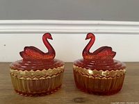 Front view of two amberina glass powder jars with lid swan finials