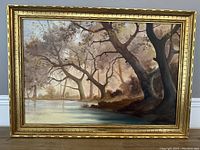 Full view of the framed oil painting showing landscape with river and trees.