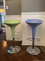 Front view of the two swivel bar stools showing green and blue seats with chrome pedestal bases and footrests.