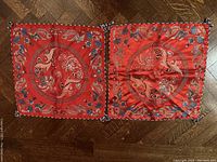 Two square red silk pillow cases spread on a wooden floor, showing circular embroidery centerpieces with dragons and phoenixes and decorative borders.