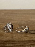 Two sterling silver ladies rings with stones, one ornate filigree with purple stone, the other with dark round stone and floral side detail, marked 925.