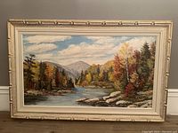 Full frontal view of signed landscape painting showing river, autumn trees, mountains, clouds, and frame.