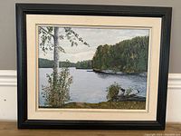 Framed oil on board painting showing a lake with forest and a birch tree in the foreground.