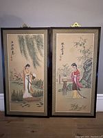 Full view of the pair of framed Asian paintings depicting traditional female figures outside in nature.