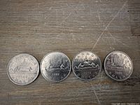 Obverse of four Canadian silver dollars showing date and Voyageur canoe design.