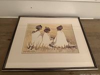 Framed art print showing three figures wrapped in white cloths sitting in grass, signed Lucy M. Wiles in lower left corner.
