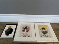 Lot of three art prints arranged side by side on wooden floor showing different themes and styles