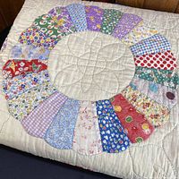 Close-up of one Dresden plate block showing variety of small floral fabric wedges sewn into cream background; hand quilting visible