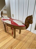 Angled front view showing wood frame with horse-head ends and attached padded saddle cushion