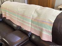 Full view of the wool blanket draped over sofa showing cream base color with pastel horizontal stripes and pink trim.