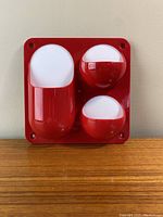 Front view of the red modular space age desk organizer showing three compartments with white backs on a square red plastic base with mounting holes at the corners.