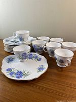Group photo showing eight plates stacked and eight matching cups arranged on a wooden surface, highlighting the blue floral pattern and gold trim.