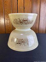 Two vintage Pyrex nesting bowls stacked upside down, each with brown mushroom and foliage design on speckled beige background.