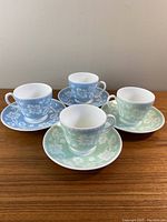 All 4 cups and saucers displayed on wooden surface, 2 green and 2 blue with white floral patterns.