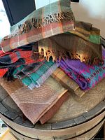 Stack of 7 scarves showing various colors and patterns including plaids and fringed edges