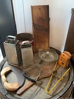 Photo of various vintage baking and kitchen tools including graters, cutting board, citrus reamer, flour sifter, wooden utensils, and other items.