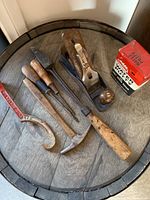 Top-down view of the antique tool lot showing wood planer, screwdrivers, pry bar, hammer, and a box of water putty on a wooden barrel top.
