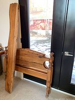 Antique wooden bed frame standing against a wall and door, with visible footboard and disassembled parts leaning alongside
