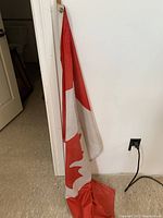 Full view of Canadian flag on its wooden stick leaning against a wall, showing the entire flag design and stick length.