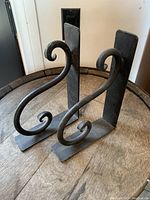 Front view of two cast iron bookends with decorative curled scrolls placed on a wooden surface.