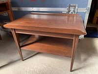 Side and front angle shot of the wooden coffee table showing table top, legs, and lower shelf.