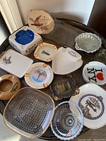 Photo showing the entire collection of 15 vintage ashtrays of various shapes, colors, and materials on a wooden surface.