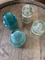 Top view of four glass hydro insulators showing two clear and two aqua blue-green insulators on a wooden surface.