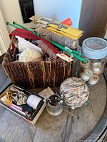 Overview of vintage sewing and knitting lot with yarn, thread, needles, zippers, pins, spools, and small hardware items in a woven basket on a wooden table.