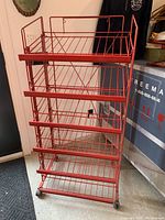 Full view of vintage red metal snack display rack showing four wire shelves and wheels.